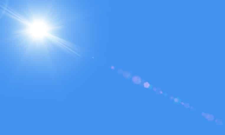 The bright white sun with rays against a blue sky without clouds. Sun is in the upper left corner. There is a sunbeams with realistic lensflare representing heat and summer.